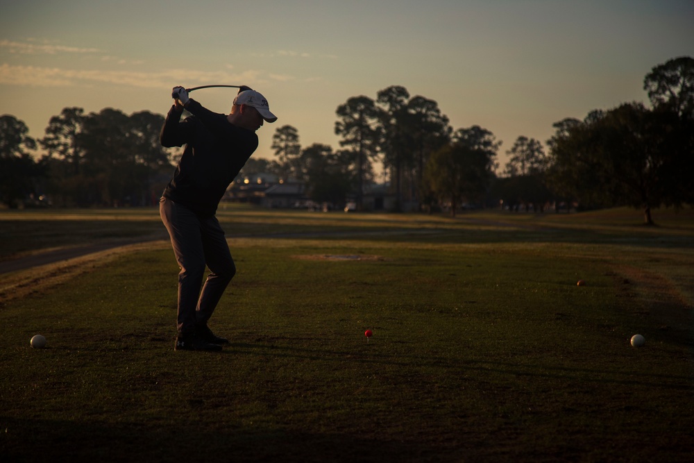 Golfer silhouetted mid-swing in follow-through at dusk on a driving range