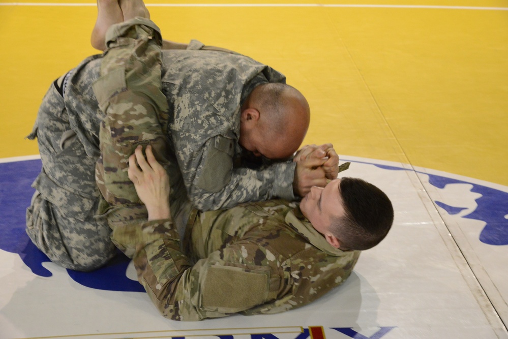 Two soldiers grappling on a wrestling mat during a combatives tournament